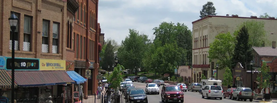Manitou Avenue in Manitou Springs: brick storefronts on the left and traffic heading down the tree-lined street